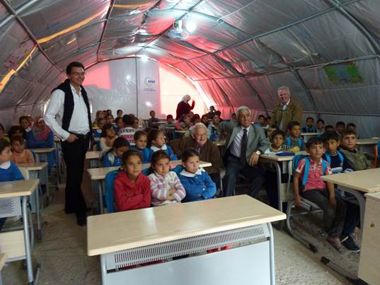 The Hon Philip Ruddock MP (centre, seated) and Mr Chris Hayes MP (standing, at right) visiting a class at Nizip refugee camp in Turkey on a parliamentary field visit, November 2014.