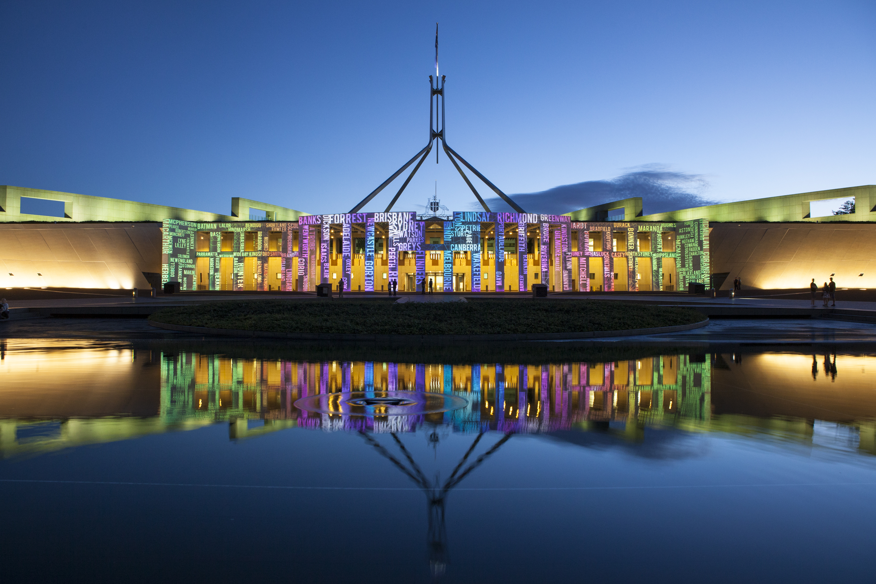 Australian Parliament House building illuminated at night, showcasing its architectural beauty and vibrant colours.
