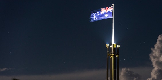 Photo of Australian flag lit up at night, flying above Australian Parliament House
