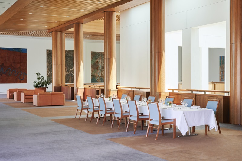 A long table covered in a white tablecloth with 12 chairs around it.