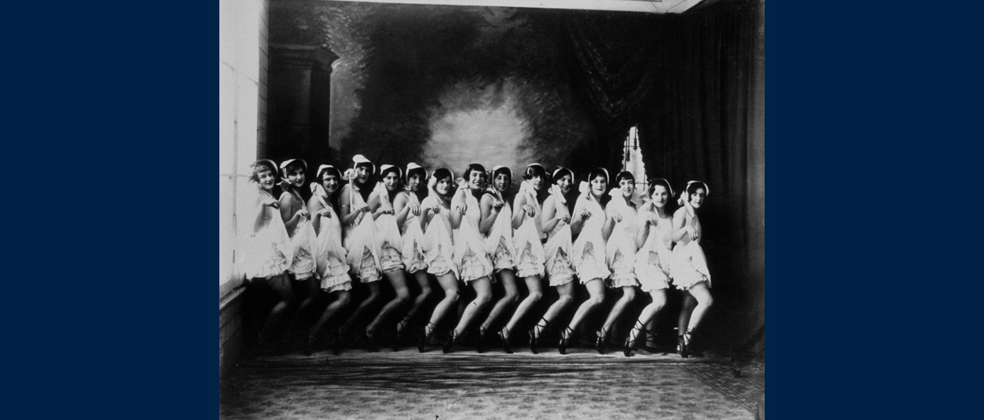 A black and white historical photograph of about 15 people lined up wearing costumes and posing